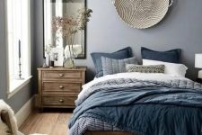 11 a chic blue bedroom with stained wooden furniture, a woven basket on the wall, blue bedding, a mirror, a boho rug and some faux fur
