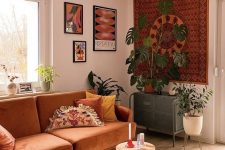 12 an earthy tone boho living room with some artwork, a rust-colored sofa, poufs and stools and potted greenery