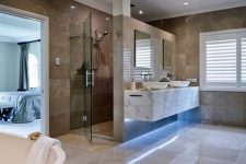 14 a large luxurious bathroom with tan and brown tiles, built-in lights, white appliances and a marble vanity