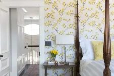 14 a vintage-inspired bedroom with yellow floral walls, a heavy bed with pillars, a chair and nightstands plus blooms
