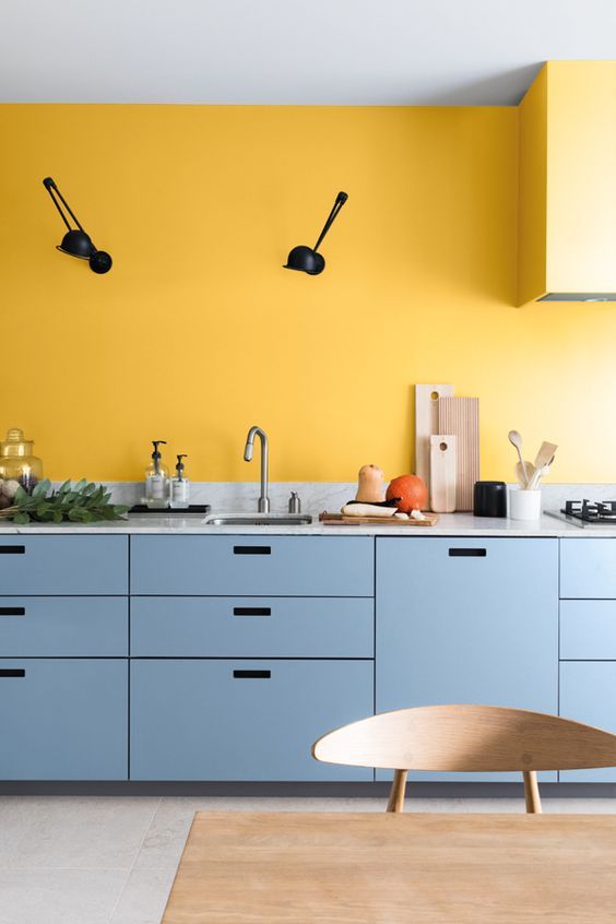 a bright one-wall kitchen with a yellow wall and blue cabinets, a hood and black fixtures and wall lamps