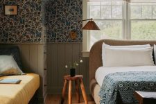 20 a vintage attic bedroom with dark floral wallpaper, a boucle upholstered bed with printed bedding, a rug and a sofa at the window