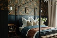 21 a moody vintage bedroom with dark floral wallpaper, a metal canopy bed, navy paneling and bedding, a crystal chandelier