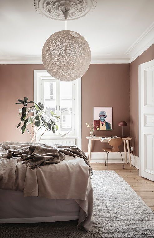 a pretty rich brown bedroom with a bed and neutral bedding, a small desk in the corner, a chair and a sphere lamp