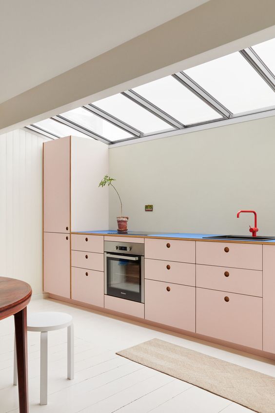 an attic kitchen with blush cabinets, a red faucet and some minimali dining furniture is a catchy space