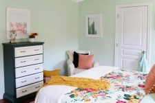 25 a mint-colored bedroom with a bed and floral bedding, a black and white dresser, a neutral chair and a chandelier
