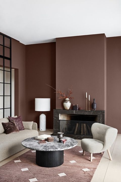 a sophisticated rich brown living room with a black marble fireplace, neutral seating furniture, a round table and vases