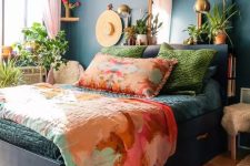 27 a bright bedroom with navy walls and a black storage bed, colorful bedding, potted plants, a mirror and brass lamps is a fun and bold space