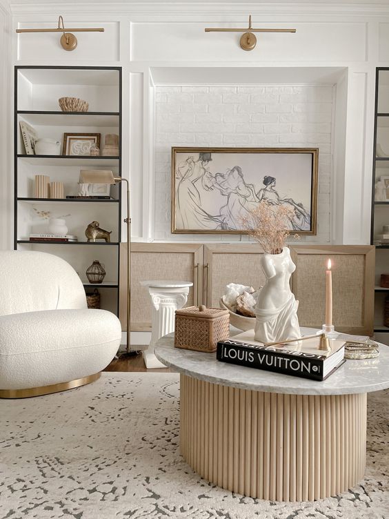 a lovely neutral living room with built-in shelves, a credenza, a rounded boucle chair and a table with a fluted base