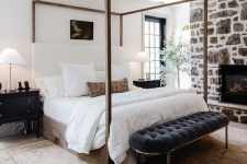 38 a modern farmhouse bedroom with a stone fireplace, a wood canopy bed, a black tufted bench, black nightstands