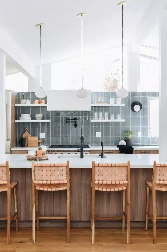 a neutral stained wooden kitchen, white shelves and a hood, a blue stacked tile wall and pendant lamps