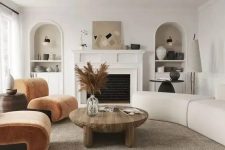39 a modern earthy living room with a fireplace, rust-colored chairs, a neutral curved sofa, a low coffee table and niches with decor