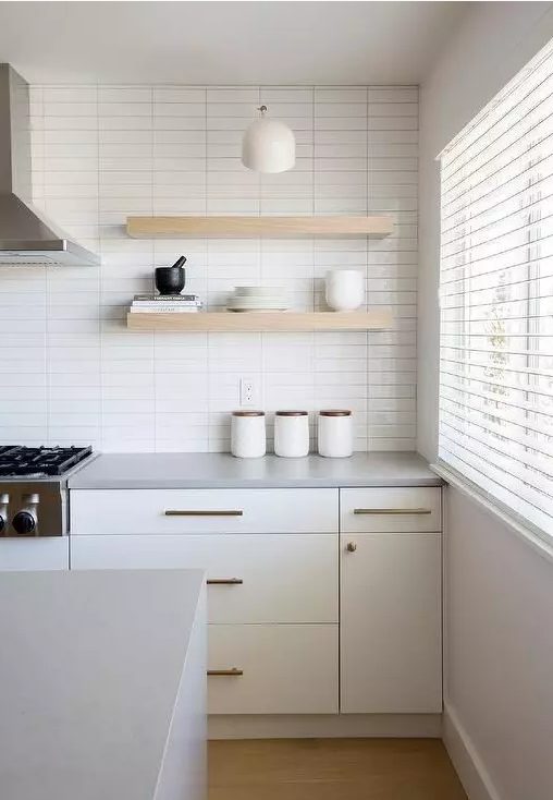 a serene white kitchen with a stacked tile wall, creamy cabinets, open shelves and brass fixtures for more chic