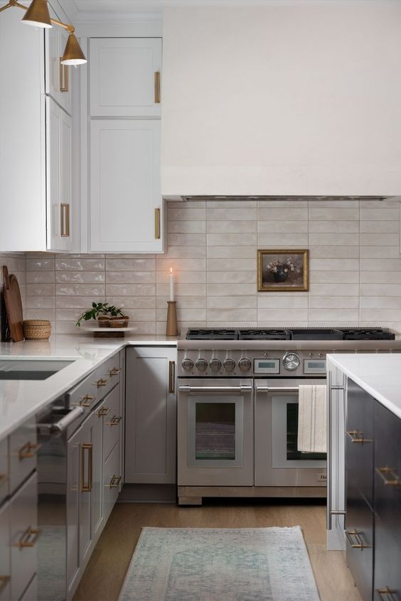 a grey kitchen with shaker cabinets, a white stacked tile backsplash and countertops and an oversized hood