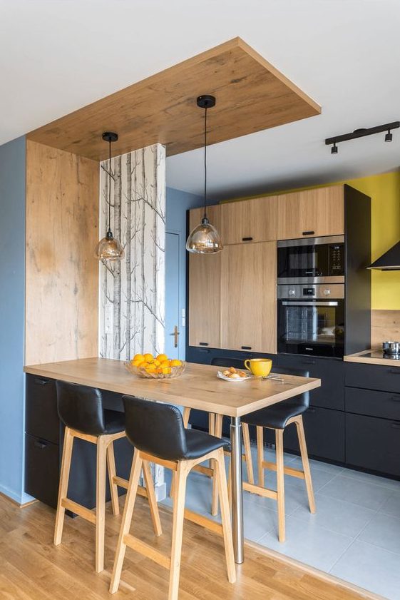 a contemporary kitchen in black and light-colored wood, with pendant lamps, black leather stools and bright yellow touches