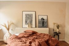 43 a warm neutral bedroom with a tan accent wall, a bed with burnt orange bedding, a copper lamp and some art