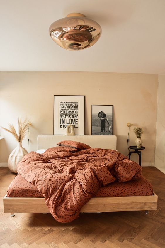 a warm neutral bedroom with a tan accent wall, a bed with burnt orange bedding, a copper lamp and some art