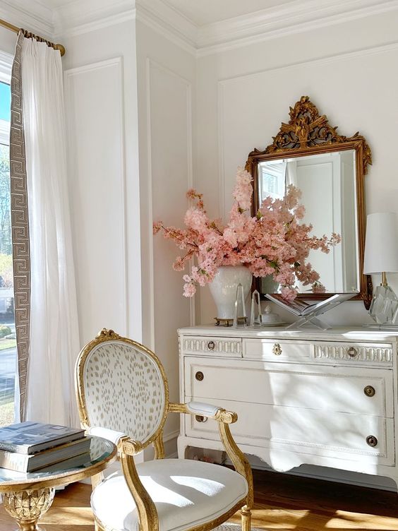 a neutral space with a vintage whitewashed sideboard and a white vintage chair, a mirror in a vintage frame
