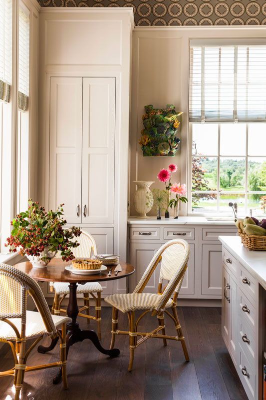 a neutral cottage kitchen with a stylish dining zone by the window, with a stained table and rattan chairs