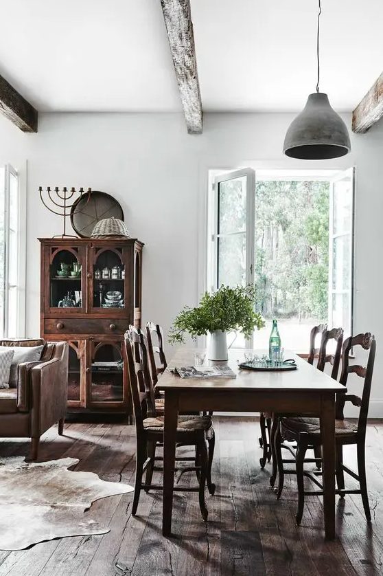 A Scandinavian dining room with dark stained furniture, a brown leather sofa, a cowhide rug and a pendant lamp