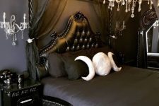 a beautiful Gothic bedroom with black walls, refined furniture, dark bedding, a crystal chandelier and wall sconces