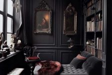 a beautiful and refined dark Gothic home library with black walls, bookcases, a soot daybed, a bench and some burgundy textiles