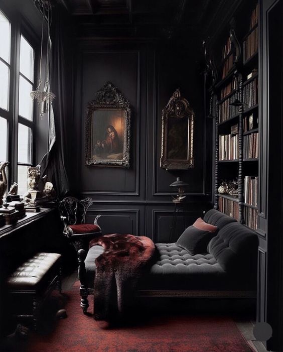 a beautiful and refined dark Gothic home library with black walls, bookcases, a soot daybed, a bench and some burgundy textiles