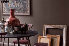 a beautiful and refined space with brown walls, a black table and burgundy chairs, a moody artwork and a chandelier