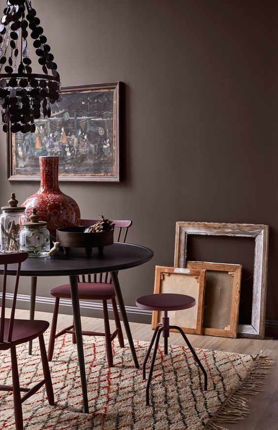 a beautiful and refined space with brown walls, a black table and burgundy chairs, a moody artwork and a chandelier