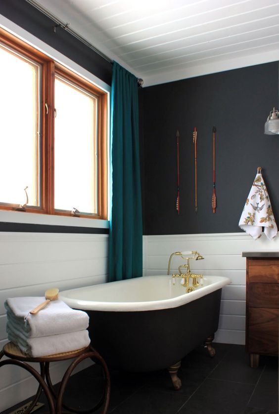 a beautiful bathroom with soot walls, white tile, a black free standing bathtub, a stool, a stained vanity and teal curtains
