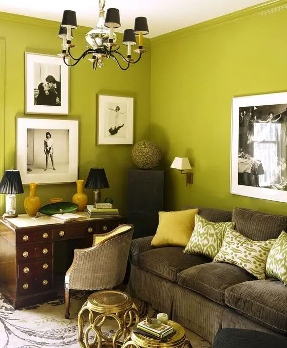 A beautiful chartreuse living room with a rich stained desk, a brown velvet sofa, printed pillows, a gallery wall and a chandelier
