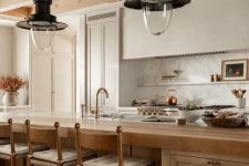 a beautiful earthy kitchen with white cabinets and a built-in hood, a large stained kitchen island, vintage pendant laps