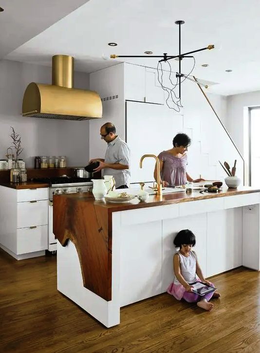 a beautiful galley kitchen with white cabinetry, living edge wood countertops and a large gold hood is wow