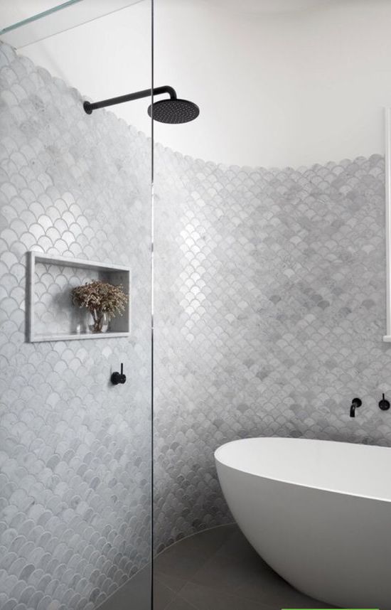 a beautiful neutral bathroom with a shower space done with silver grey fish scale tiles all over, an oval tub and black fixtures