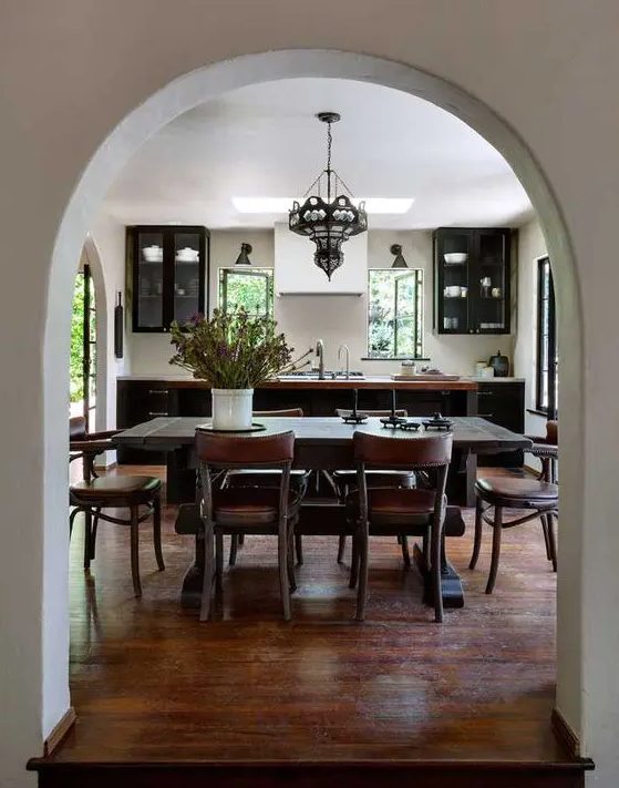 A black kitchen with a kitchen island, a dark stained dining table and brown leather chairs, a vintage chandelier