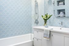 a blue fish scale tile bathroom with a navy subway tile floor, a white vanity, a tub and some towels