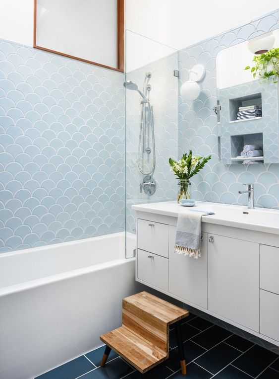 a blue fish scale tile bathroom with a navy subway tile floor, a white vanity, a tub and some towels
