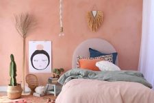 a boho bedroom with a Peach Fuzz wall, a bed with colorful bedding, some decor and potted plants