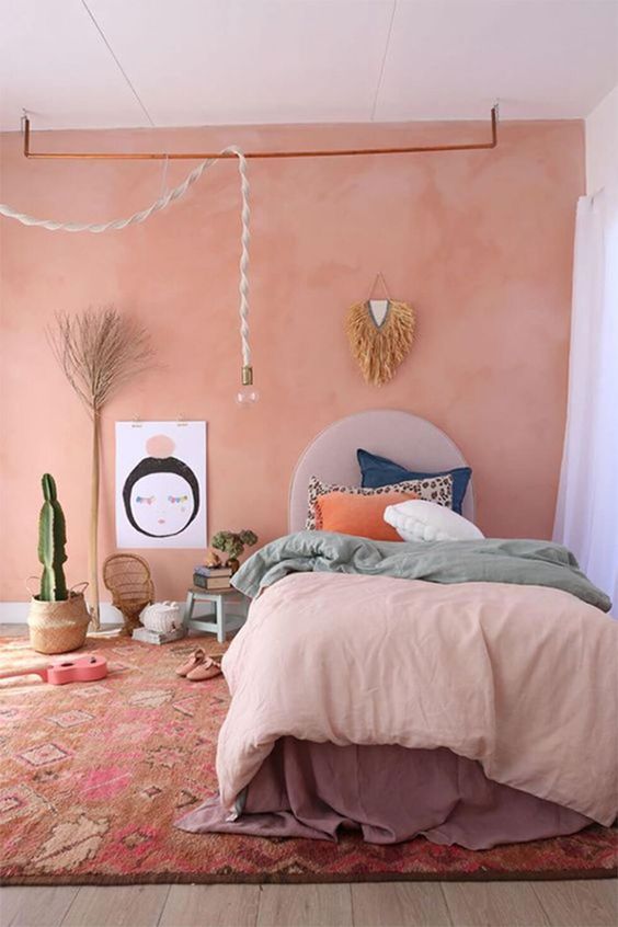 a boho bedroom with a Peach Fuzz wall, a bed with colorful bedding, some decor and potted plants