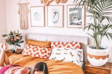 a boho girl’s bedroom with a grey upholstered bed, bright bedding, stained nightstands, a potted plant and a cool gallery wall