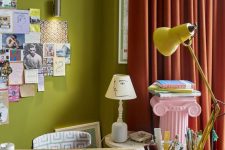 a bold home studio with chartreuse walls, a desk, a printed chair, a yellow lamp and red curtains plus a memo board