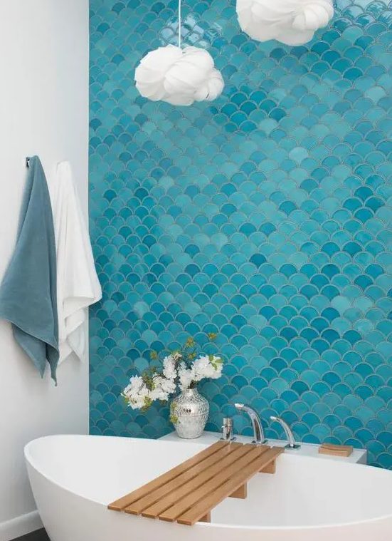 a bold modern bathroom inspired by the sea, with a blue and turquoise fish scale tile wall, an oval tub, cloud like pendant lamps