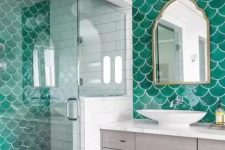 a bright bathroom with emerald fishscale tiles, a whitewashed vanity, a mirror, a sink and some lights on the wall
