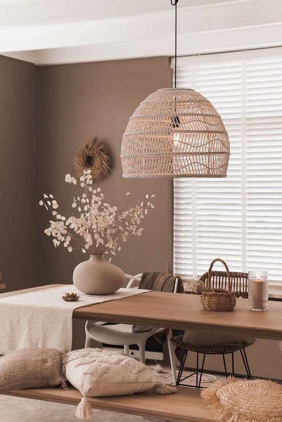 a catchy brown dining room with a stained table, mismatching chairs and a bench, a woven pendant lamp and some decor
