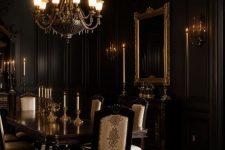 a chic Gothic dining room with black walls, a dark vintage table and neutral chairs, a fireplace, an oversized mirror and a chic chandelier