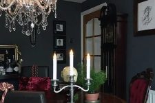 a chic Gothic kitchen with black walls, a round table, burgundy chairs, a crystal chandelier, potted greenery and artworks