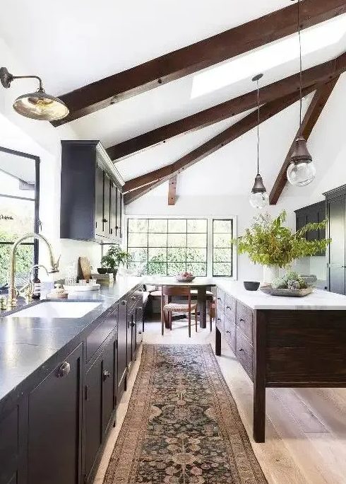 a chic modern farmhouse kitchen with a light-stained floor, dark wooden beams and a kitchen island that dominate over the space