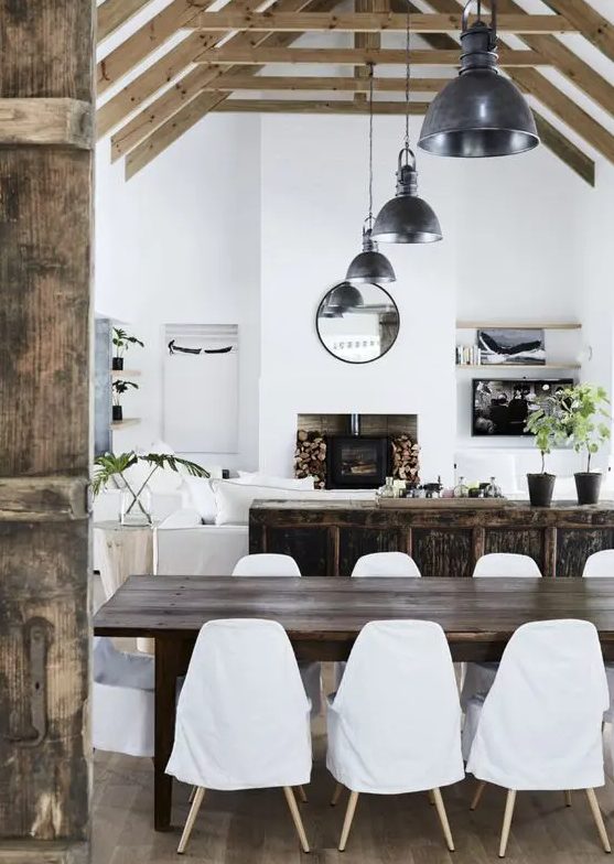 A chic open layout with a dark stained cabinet, a dark stained dining table, white seating furniture and industrial lamps