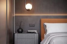 a chic taupe bedroom with a slab accent wall, an amber leather bed, a dark taupe nightstand, built-in lights and pendant lamps