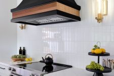 a chic white kitchen with a white stacked tile backsplash, an oversized vintage black hood that stands out in the space